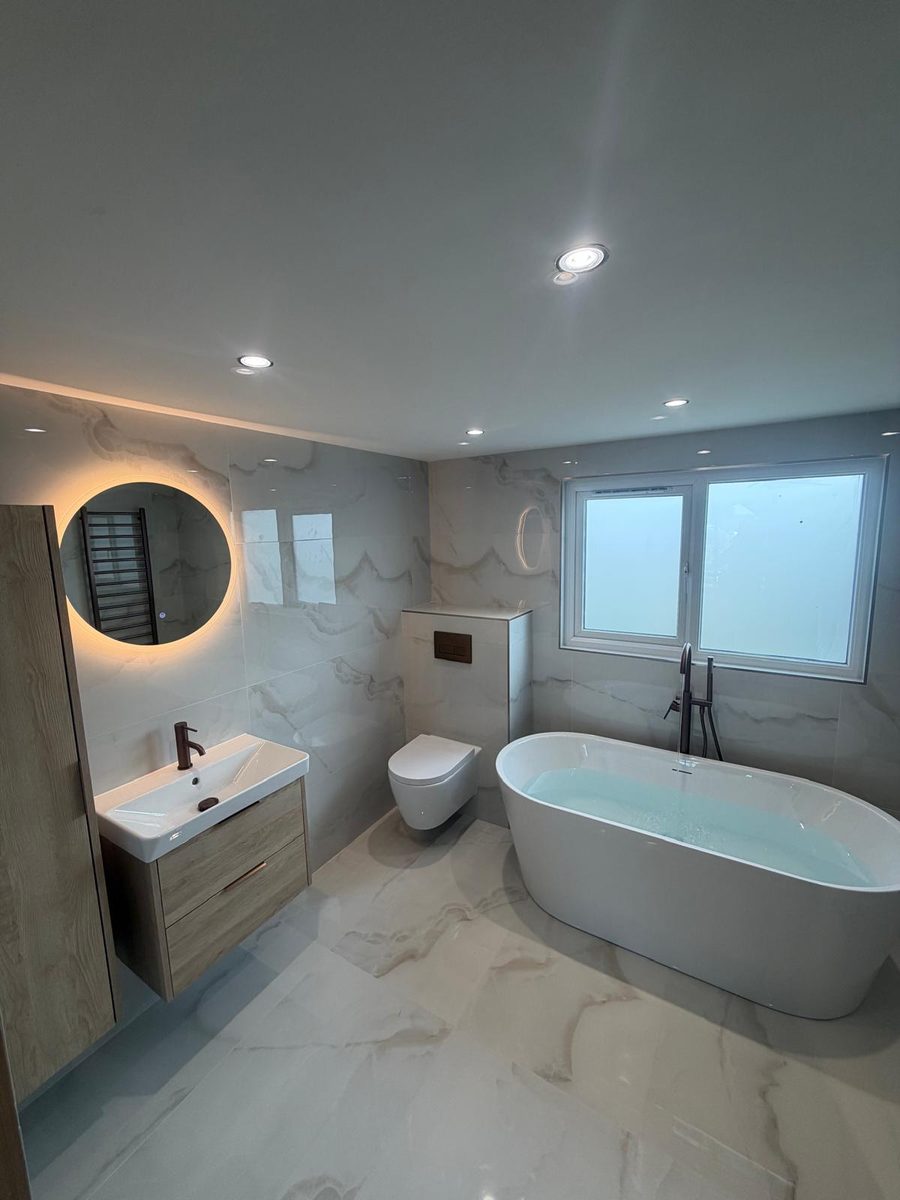 Bathroom refit in Leigh — freestanding bath, wall-hung WC and backlit round mirror, by Flow Heat Plumbing & Heating